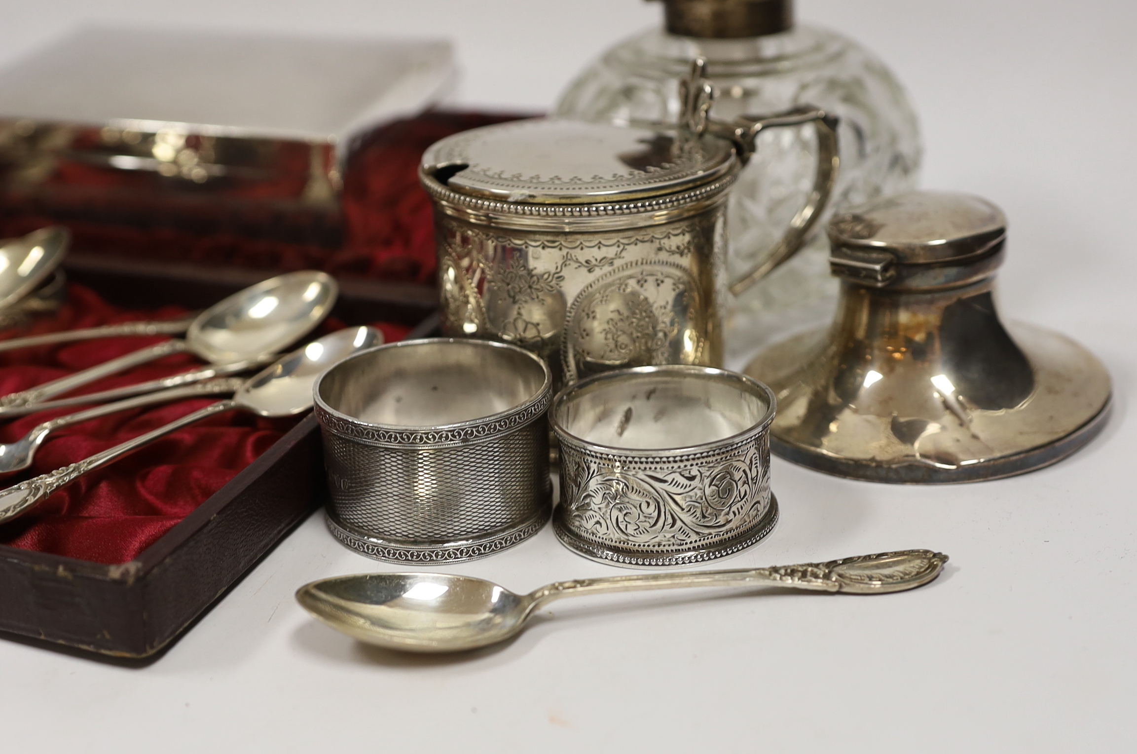 A Victorian silver mustard pot (no liner), a cased set of twelve silver teaspoons and tongs, two silver cream jugs, mounted glass scent bottle, napkin rings etc.